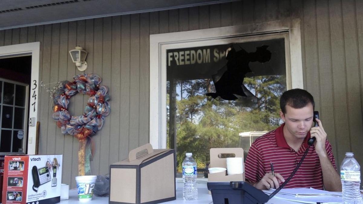 Blake Halsey, a 21-year-old college student and volunteer at the Orange County GOP office, takes a phone call from someone offering to volunteer on Monday, Oct. 17, 2016 in Hillsborough, N.C. Halsey sits under the window where authorities say someone threw in a flammable device that burned the campaign office.