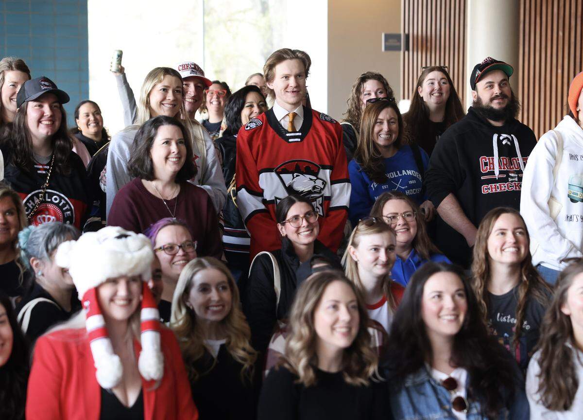 Charlotte Checkers hockey player Gracyn Sawchyn, center in red, poses with a large group of book club members Friday, March 13, 2026 before the game against the Bridgeport Islanders at Bojangles Coliseum in Charlotte.