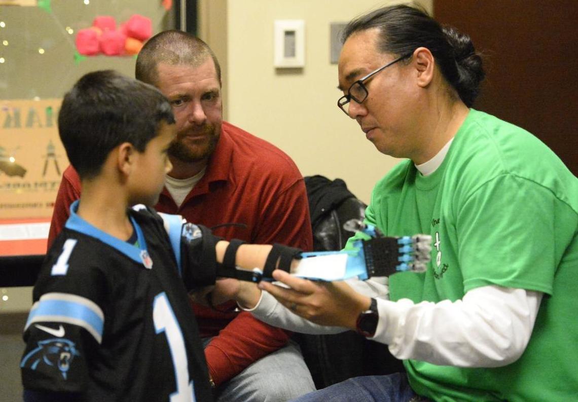 Richard Chi, a UNCC biologist who is advisor to the school’s Helping Hand Project chapter, fits a 3D-printed arm to 7-year-old Joel Payne.