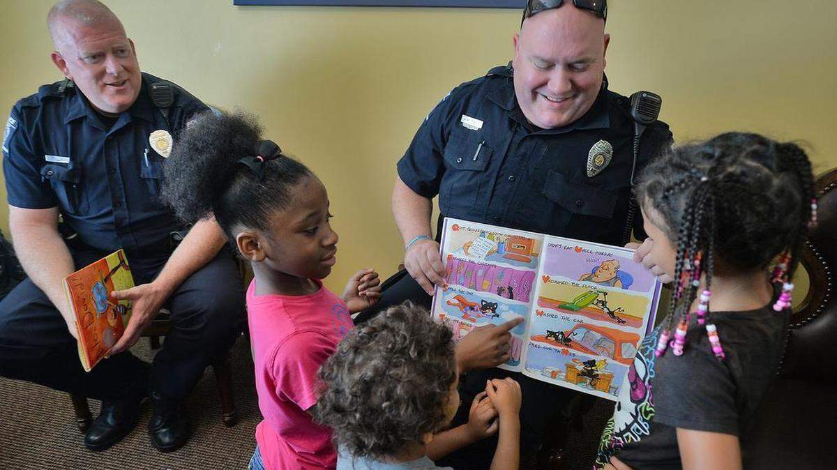 
CMPD officer Brian Russell, left, watches as officer Mike Travis laughs with the kids while holding the book “Bad Kitty.” As a community service project in its first year, Charlotte-Mecklenburg police officers in partnership with Woodstone Apartments have made a strong connection with the residents and especially the youth. During the summer months CMDP officers mentored the youth through reading and other activities. 
