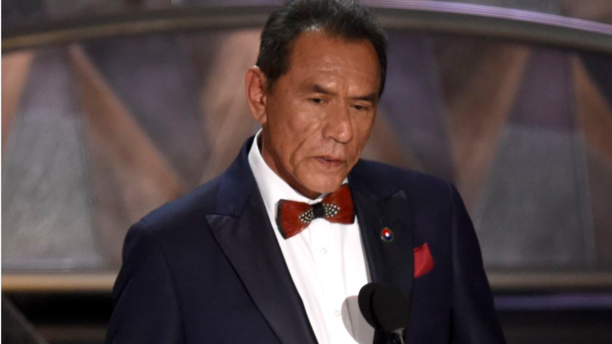 Wes Studi at the podium, as he speaks Cherokee native language, during Oscars.