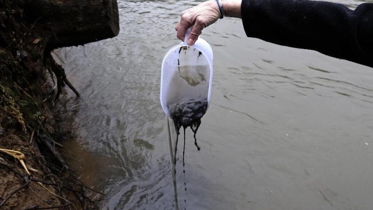 An official of the Dan River Basin Association scoops coal ash from the banks of the river in this 2014 photo.