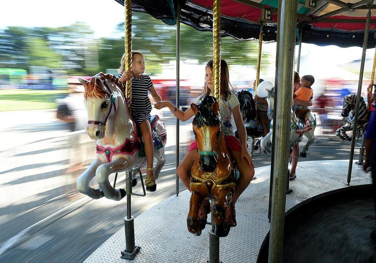 Sisters Anna Kaplan, left, 4, and Emery Kaplan, 7, hold hands as they ride the Brinkley Entertainment antique merry-go-round at Saturday’s Matthews Alive Festival. The annual festival, which runs through Monday, is dedicated to the support of local non-profit organizations. This is its 25th anniversary.