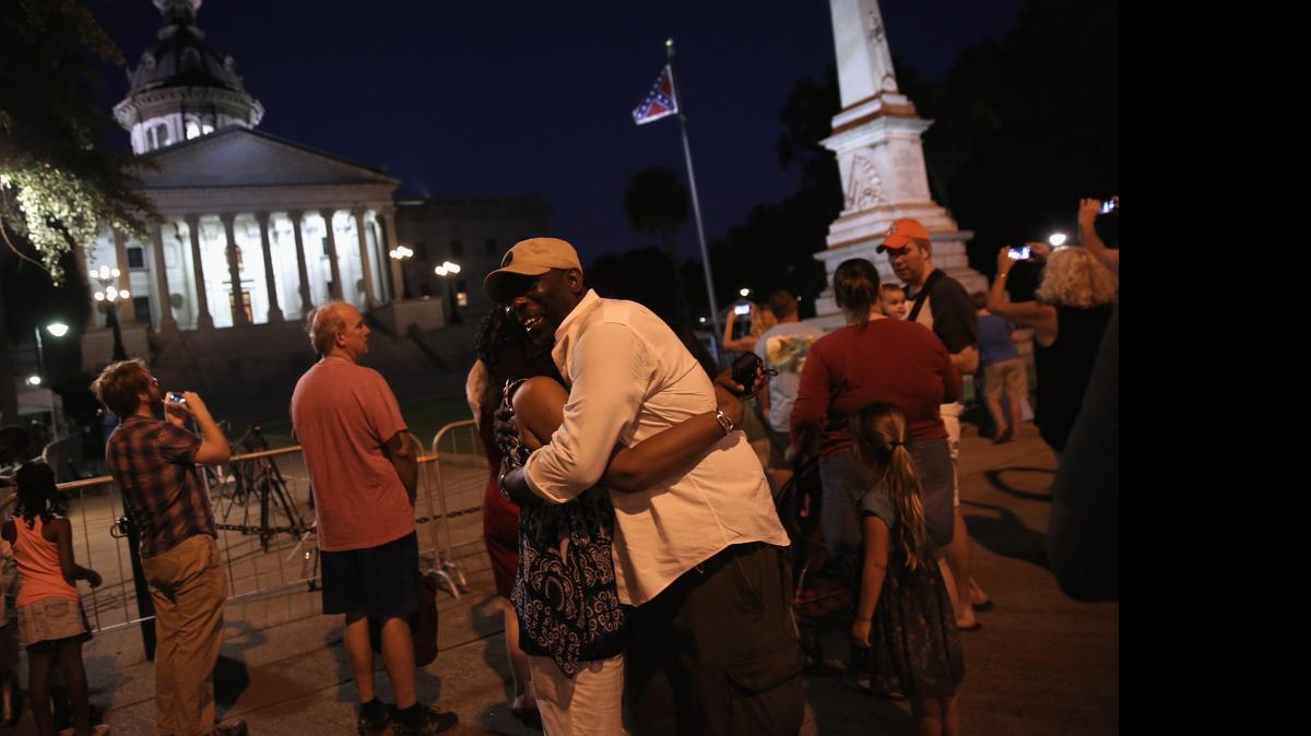 
COLUMBIA, SC - JULY 09: A couple embraces as the Confederate flag flies in front of the South Carolina statehouse on its last evening on July 9, 2015 in Columbia, South Carolina. South Carolina Governor Nikki Haley signed a bill to remove the Confederate flag from the statehouse grounds Friday morning. 
