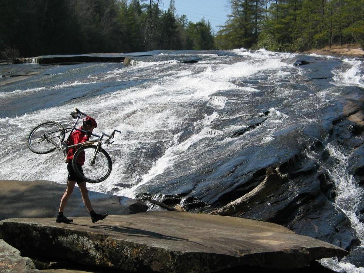 A mountain biker picks his way across a boulder at Bridal Veil Falls in DuPont State Forest.