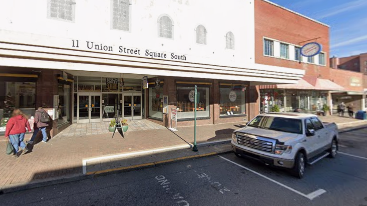 A wide, daytime photo of a two-story building in a downtown area, with the address “11 Union Street Square South” clearly visible above a row of glass double doors. A white Ford pickup truck is parked on the street in front of the building, and two people are walking toward the entrance on the brick sidewalk.