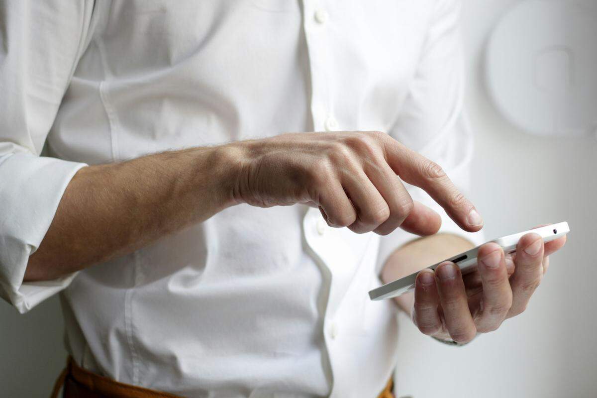 A person wearing a white shirt holds a smartphone in one hand and uses a finger from the other hand to swipe on the screen. The focus is on the hands and the phone, with the background blurred.