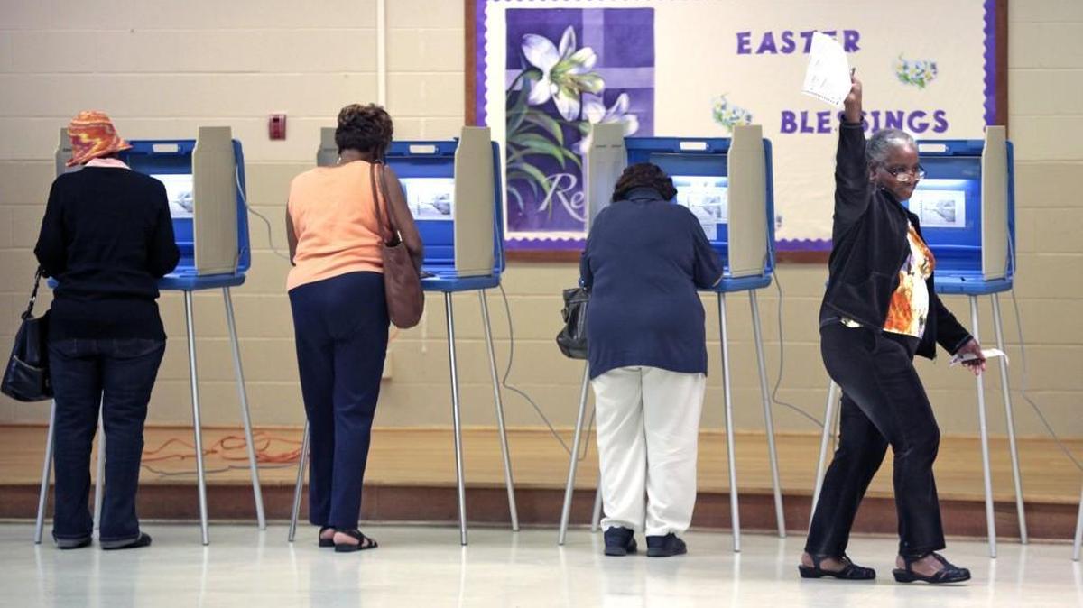 At right, a voter waves her completed ballot to a poll worker as she moves toward the vote counting machine at the White Rock Baptist Church precinct on Fayetteville Road, Durham, NC Tuesday, March 15, 2016.