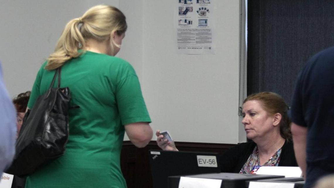 A Wake county voter at left shows her ID to a registration official at the Herbert C. Young Community Center early voting site in Cary, NC Friday, March 11, 2016.