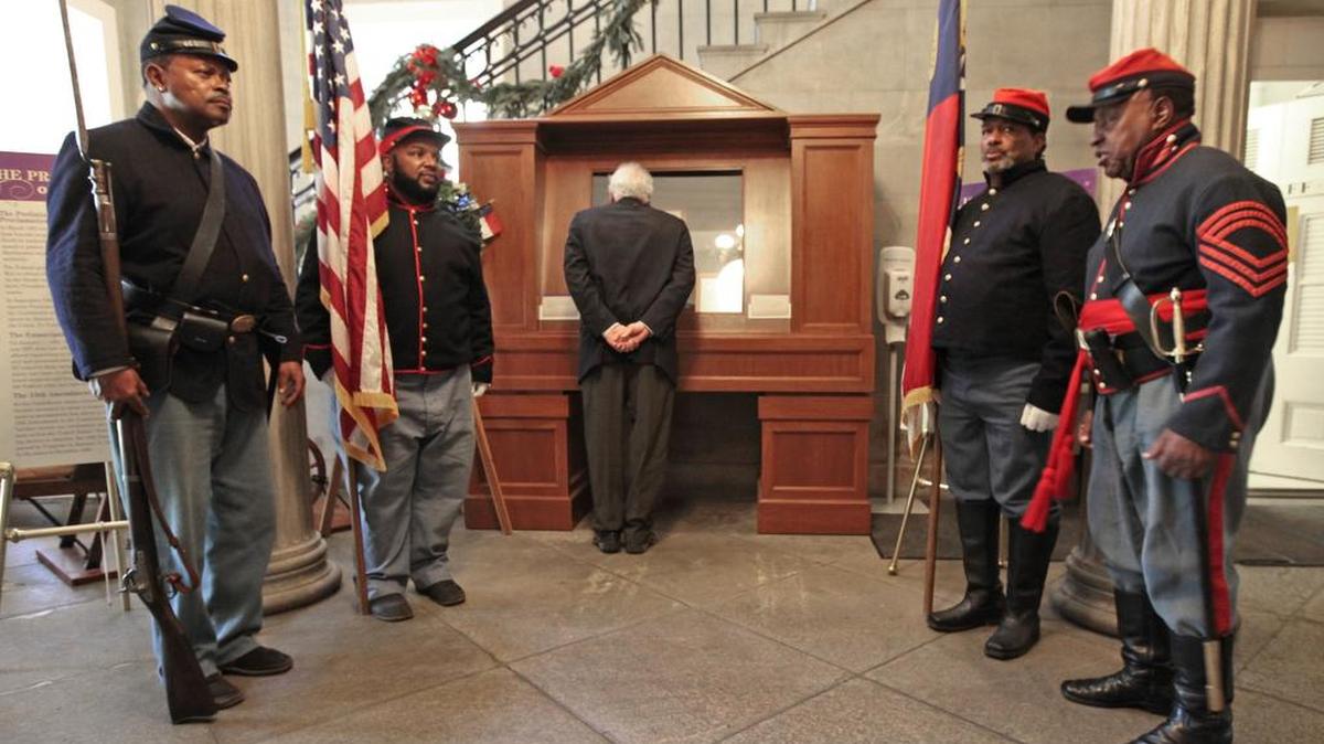 From left, Civil War color guard reenactors Bernard George, Tom Hancock, Youngs Leff and Marvin Nicholson stand as an honor guard in the NC State Capitol while a visitor, center, gets a closer look at the state of North Carolina's original copy of the Thirteenth Amendment to the US Constitution Friday, December 4, 2015. Friday, December 4, 2015 is the 150th anniversary of the state's ratification of the 13th Amendment prohibiting slavery and involuntary servitude and the enforcement of this law by appropriate legislation. A commemoration ceremony was held prior to this in the NC State House chamber at the Capitol, where the original document was signed 150 years ago today. The color guard reenactors were representing the 35th, 36th and 37th US Colored Troops Infantry and the 14th Heavy Artillery from the Civil War.