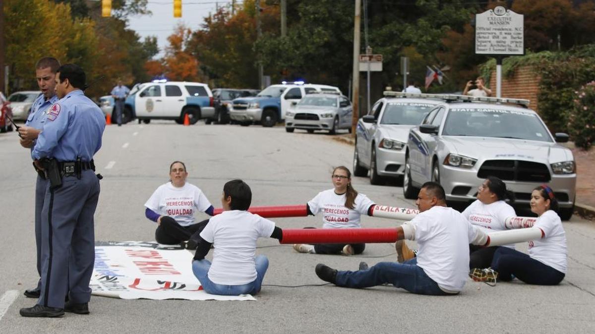 Raleigh Police officers at left confer while a group of six immigration protestors who shackled themselves together and ran out to sit down blocking North Blount Street in front of the NC Governor's Mansion Thursday, October 29, 2015. The protesters were eventually cut apart and individually arrested and removed from the street. The immigration protestors were part of a larger very vocal crowd on the sidewalk protesting NC Governor Pat McCrory's signing Wednesday of HB318, tightening immigration laws in NC.
