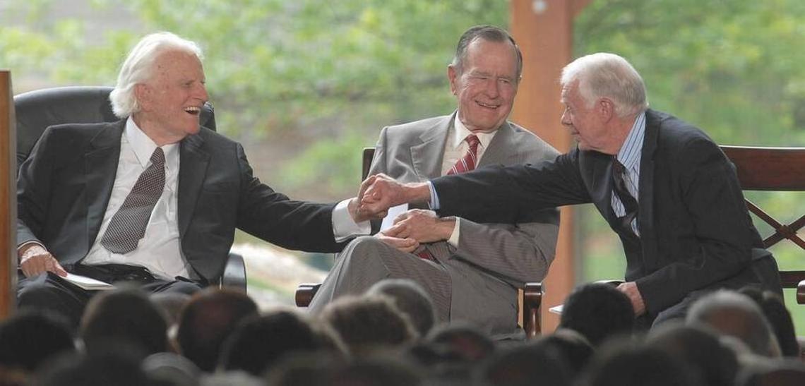 Billy Graham shakes hands with Jimmy Carter as George H.W. Bush looks on, at the Billy Graham Library in 2007.