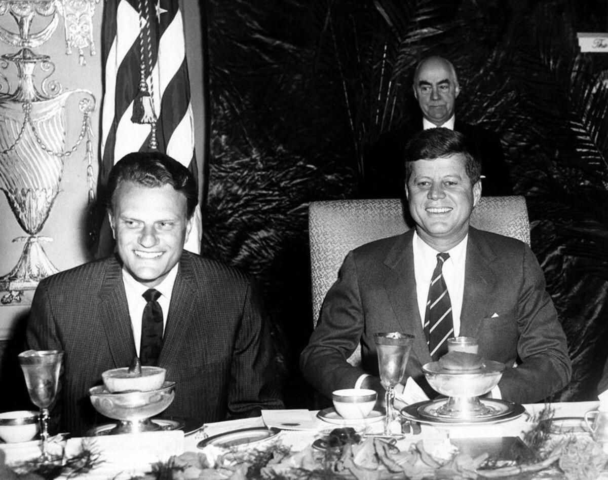 Seated at the head table, next to President John F. Kennedy, Graham appears at a prayer breakfast, sponsored by the International Council for Christian Leadership, at the Mayflower Hotel in Washington D.C.