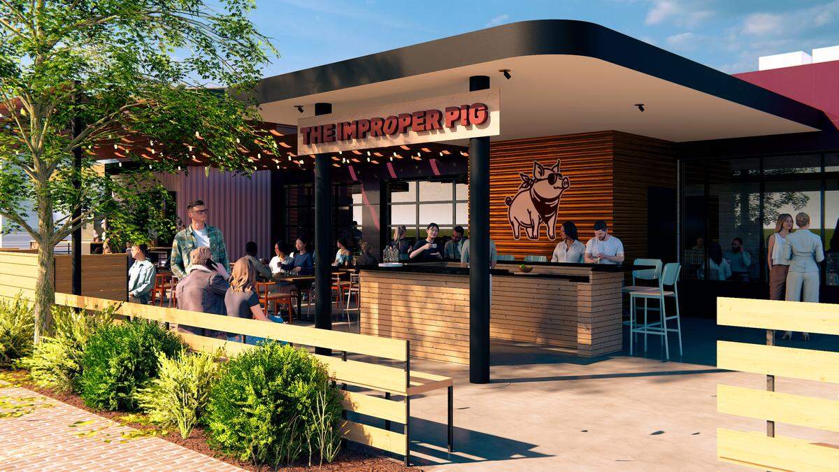 A digital rendering of the restaurant “The Improper Pig” shows an outdoor patio with a bar and several tables where people are seated. The building has a modern design with wood siding, a flat roof, and a logo of a pig wearing sunglasses.