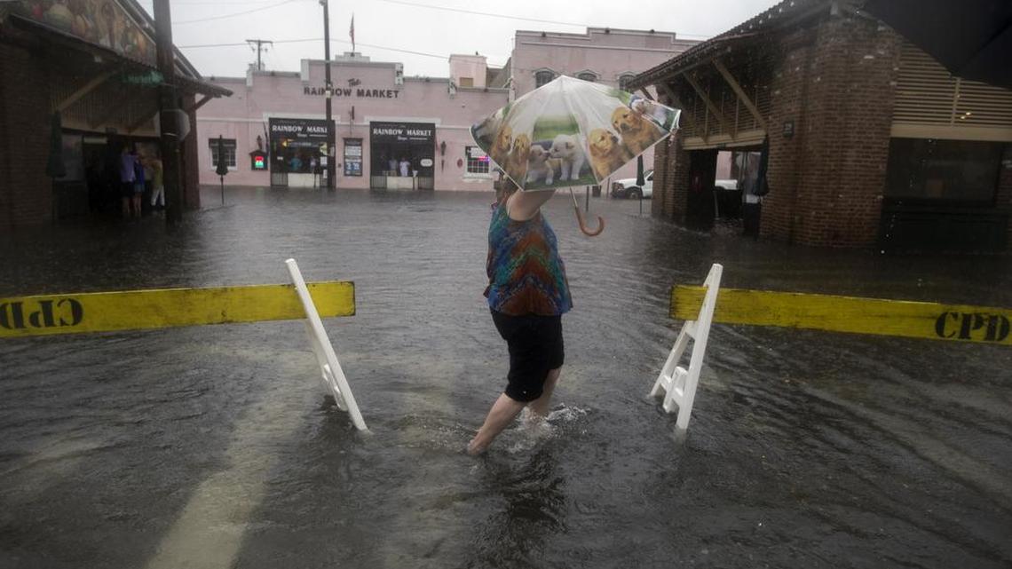 In this Thursday, Oct. 1, 2015 photo, a pedestrian walks past two barriers in place to stop vehicles from driving through the flooded streets of City Market in Charleston, S.C. Heavy thunderstorms can leave intersections impassable like the streets flooded near Charleston’s City Market area, a popular tourist haunt.