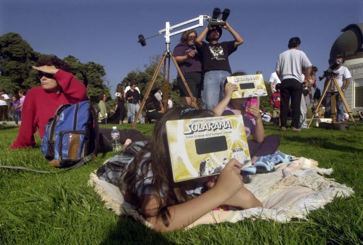 In this June 10, 2002, file photo, Lise Richardson, left, views a partial solar eclipse with her daughters Sophia Richardson, center left, and Samantha, 6, right, at Griffith Observatory in Los Angeles. Destinations are hosting festivals, hotels are selling out and travelers are planning trips for the total solar eclipse that will be visible coast to coast on Aug. 21, 2017. A narrow path of the United States 60 to 70 miles wide from Oregon to South Carolina will experience total darkness, also known as totality.