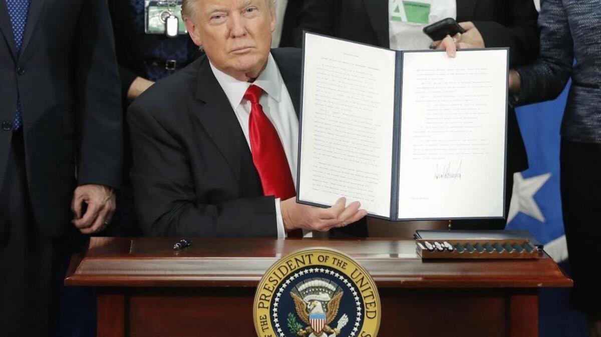 President Donald Trump holds up an executive order for border security and immigration enforcement improvements after signing the order Wednesday during a visit to the Homeland Security Department headquarters in Washington.