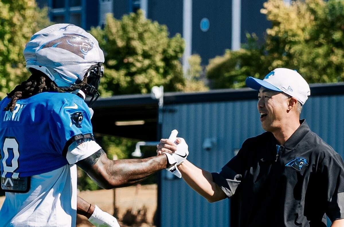 George Li, right, and Carolina Panthers defensive back Jaycee Horn are pictured dapping up at a practice. Li is the team’s game management coordinator.