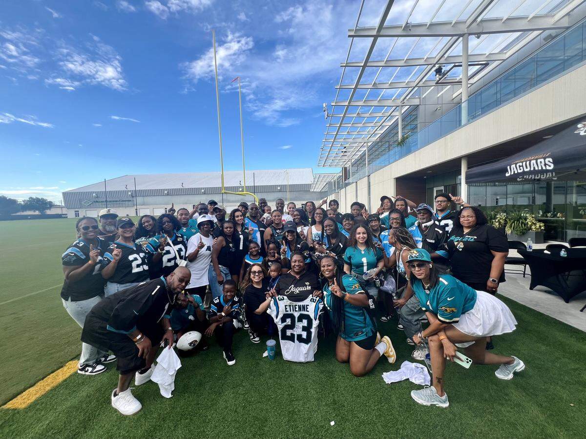The family of Travis Jr. and Trevor Etienne, all wearing customized Jaguars and Panthers jerseys, gather outside EverBank Stadium to take a photo after the game.