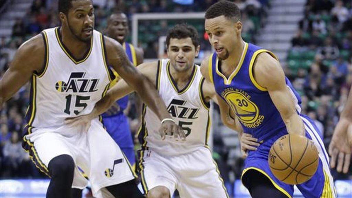 Golden State Warriors guard Stephen Curry (30) drives around Utah Jazz's Derrick Favors (15) and Raul Neto, center, in the first quarter during an NBA basketball game Monday, Nov. 30, 2015, in Salt Lake City.