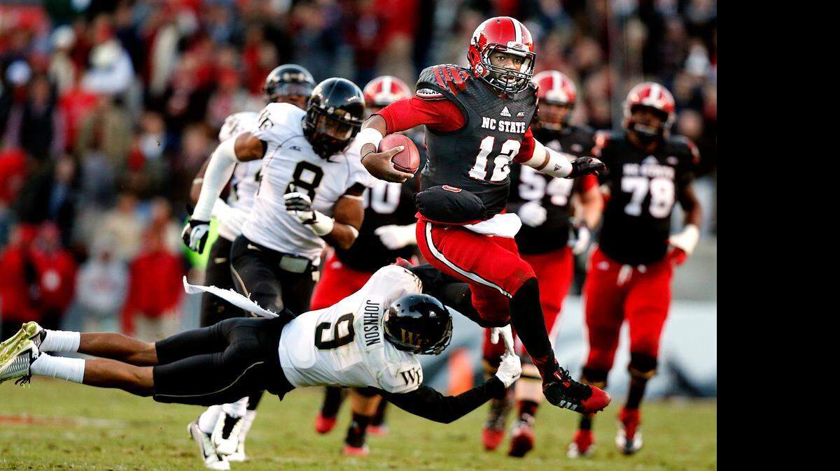
N.C. State quarterback Jacoby Brissett (12) avoids the tackle of Wake Forest cornerback Kevin Johnson (9) on a long run during the first half of the Wolfpack's game against Wake Forest at Carter-Finley Stadium in Raleigh, N.C., Saturday, Nov. 15, 2014.
