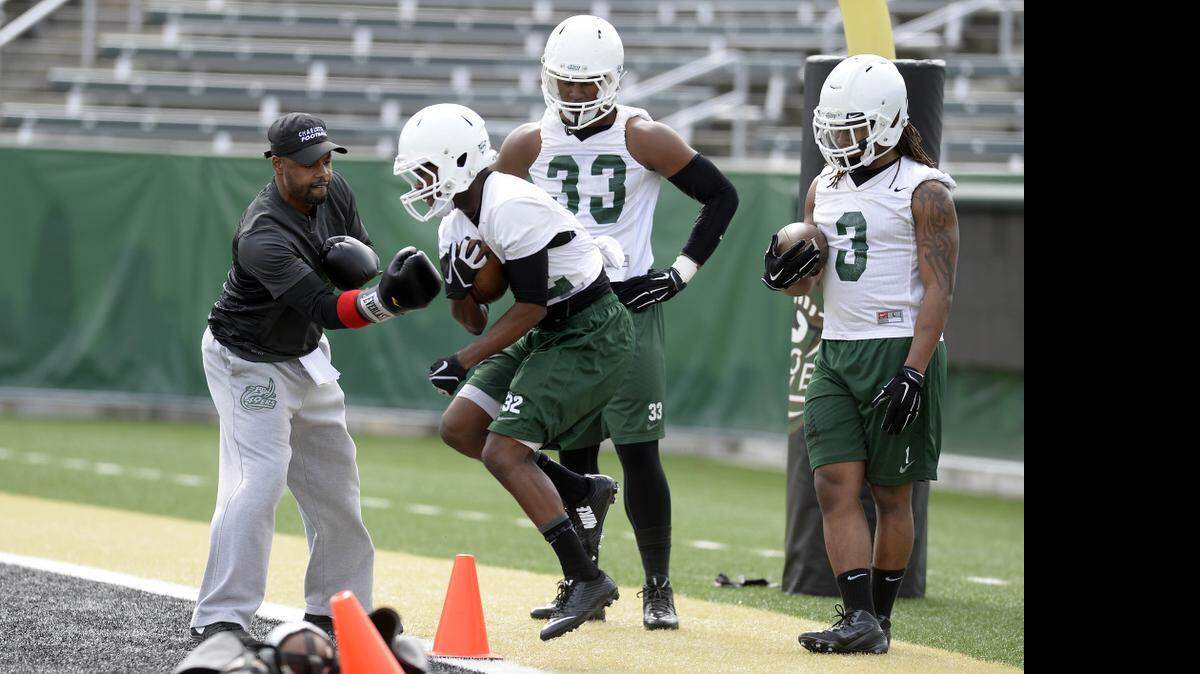 
Charlotte 49ers' running backs coach Damien Gary, left, uses boxing gloves to try to punch the ball out of the hands of Damarrell Alexander (32), as Garrison Duncan (33), and Kalif Phillips (3) wait their turn during the first day of Charlotte 49ers' spring football practice at Jerry Richardson Stadium on March 14, 2015.
