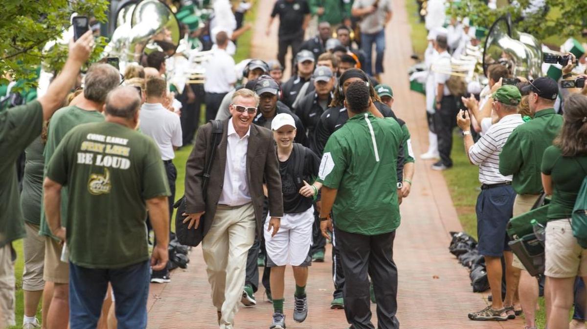 
Charlotte 49ers football coach Brad Lambert (smiling) enters Richardson Stadium with his team before Saturday’s home opener against Presbyterian. Charlotte won 34-10.
