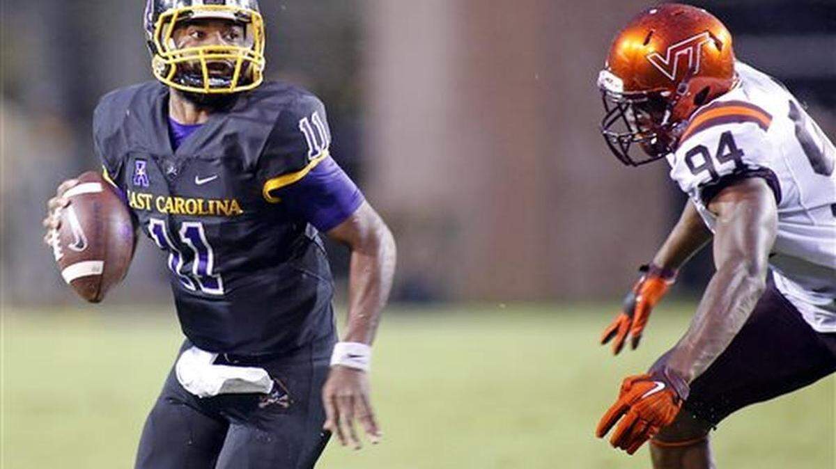 
East Carolina's James Summers (11) looks to pass the ball while being pursued by Virginia Tech's Trevon Hill (94) during the second half of an NCAA college football game in Greenville last week. East Carolina won 35-28.
