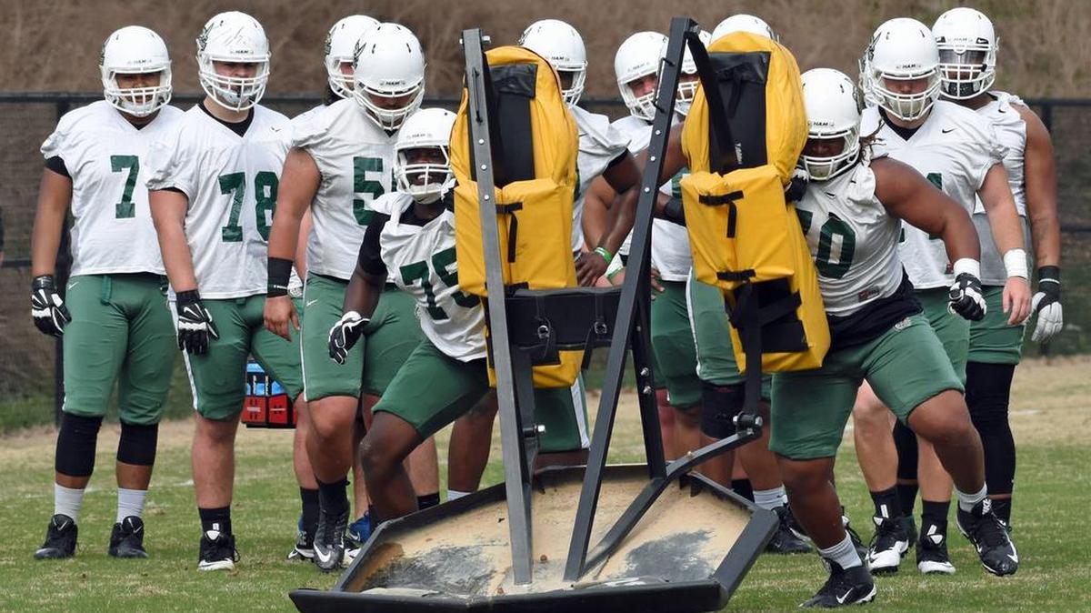 Charlotte offensive linemen Eugene German (75) and Casey Perry (70) hit the blocking sled as teammates watch during the 49ers’ first spring practice Saturday morning. Charlotte will practice three days a week until its annual Green-White Spring Game on April 23 at Richardson Stadium.