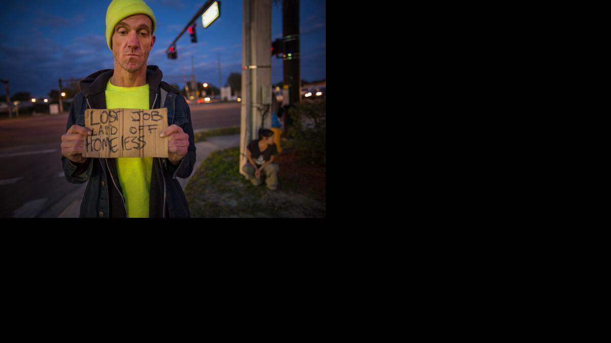 
Ryan Hoffman with a panhandling sign and his girlfriend Michelle Pettigrew, in background, at a busy intersection in Lakeland, Fla., Jan. 7, 2015. Hoffman, once a 287-pound starting left tackle for a top-ten ranked University of North Carolina football team, renowned for his toughness and durability, is now plagued with short-term memory problems and lives on the street, sometimes begging money from passing cars.
