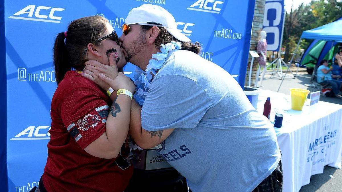 
Opposing team husband and wife, Katrina and Coby Carter from Gastonia, kiss after battling over who will win the Belk trophy. Thousands of North Carolina and South Carolina fans gathered uptown for the Belk College Kickoff Game at Bank of America Stadium.
