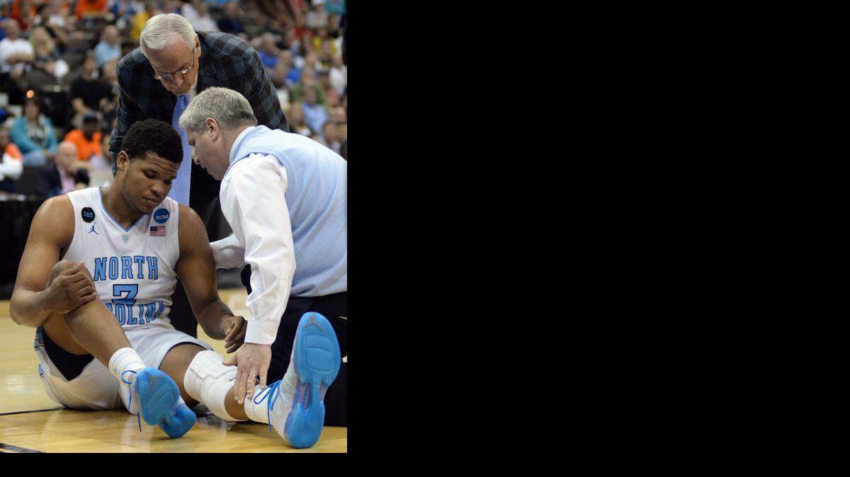 
North Carolina head coach Roy Williams, background, looks on a trainer helps forward Kennedy Meeks after he injured his knee during the second half of an NCAA tournament third round basketball game against Arkansas Saturday, March 21, 2015, in Jacksonville, Fla. 

