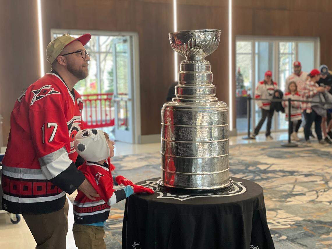 Hundreds of fans, including the two pictured here decked in Carolina Hurricanes gear, visit Bojangles Coliseum on Saturday, December 21, 2024, to take a photo with the Stanley Cup before the Charlotte Checkers game.