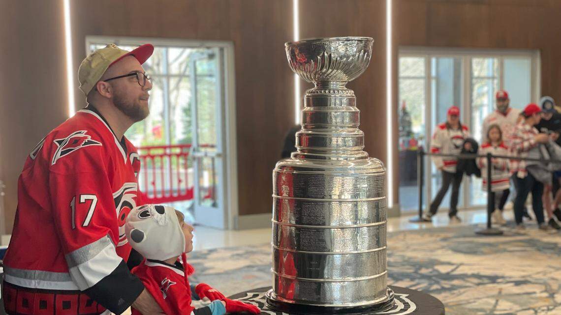 Hundreds of fans, including the two pictured here decked in Carolina Hurricanes gear, visit Bojangles Coliseum on Saturday, December 21, 2024, to take a photo with the Stanley Cup before the Charlotte Checkers game.