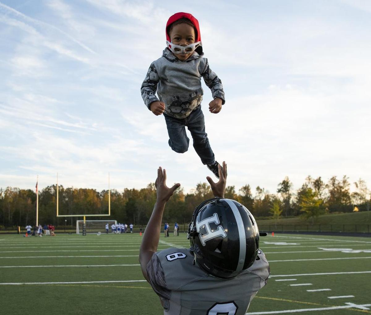 Hough’s Mario Love tosses 3-year-old Apollo Thompson in the air during warmups before facing North Meck at a high school football game at Hough. Laramie Thompson, Apollo’s father, is the Huskies’ wide receivers coach.