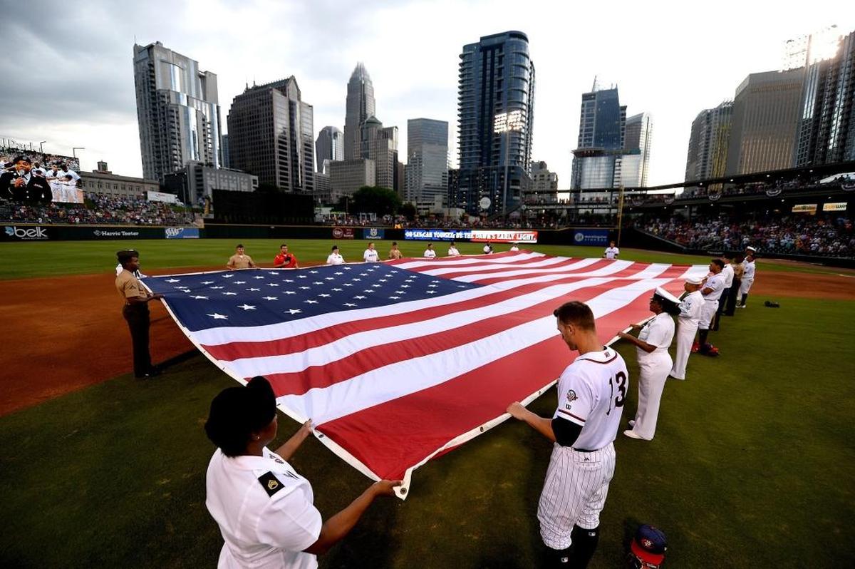 Military personnel and members of the Charlotte Knights baseball team hold an American flag in the BB&T BallPark infield during the singing of the national anthem before a game last summer.