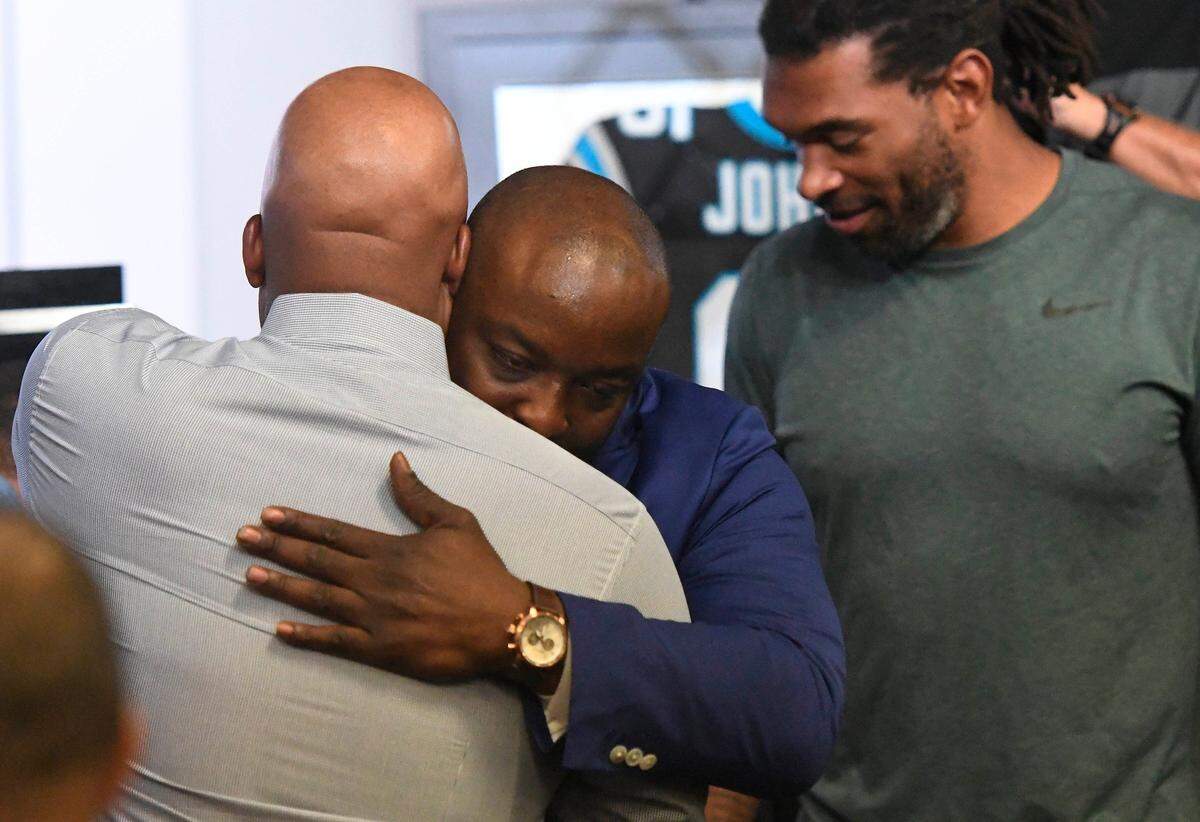 Former Carolina Panthers defensive end Charles Johnson, who is second all-time in sacks in the the franchise's history, hugs defensive coordinator Eric Washington, as Julius Peppers waits, after a retirement press conference at Bank of America Stadium on Thursday, August 23, 2018.