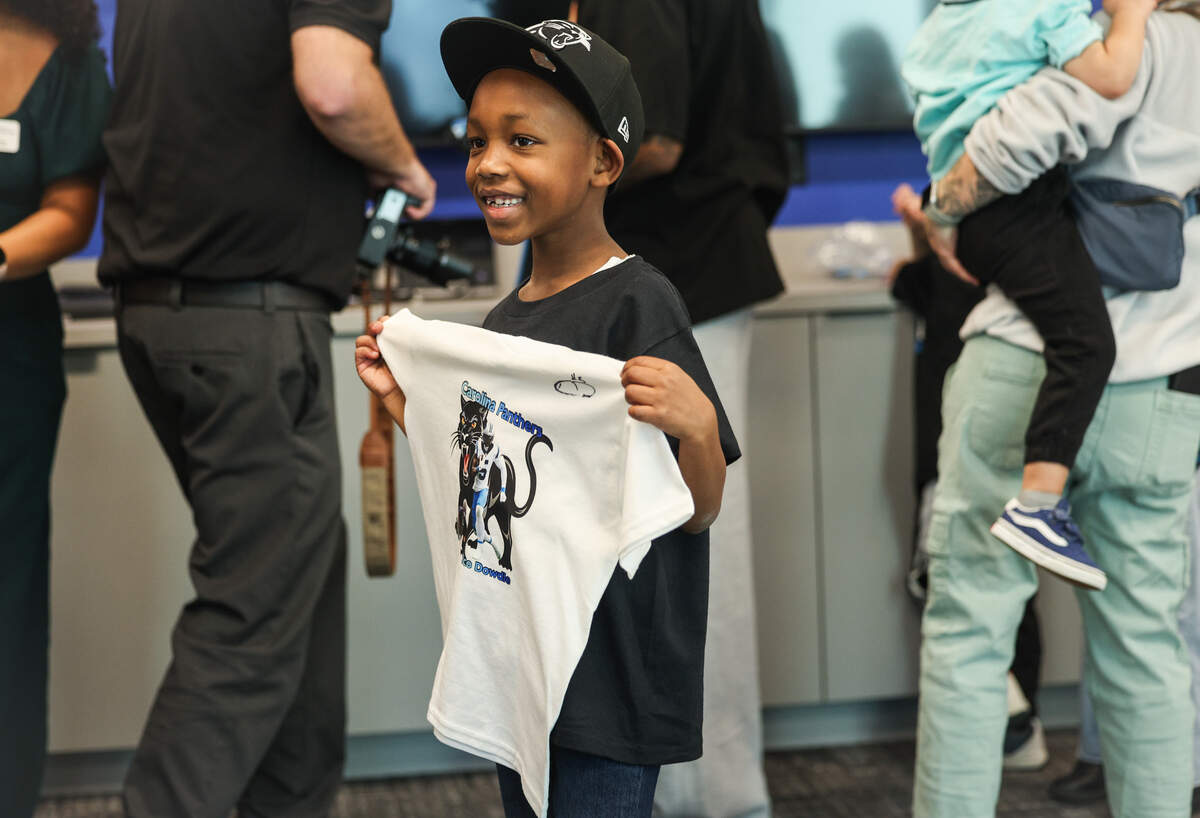 Aaron Wright, II, 7, is all smiles as he holds a T-shirt autographed by Panthers running back Rico Dowdle during a visit to Children’s Home Society of North Carolina (CHS) in Charlotte on Friday, Nov. 14, 2025. Dowdle presented CHS with a check for $45,000 as he turned a penalty into purpose, transforming a fine for his touchdown celebration into a charitable cause.