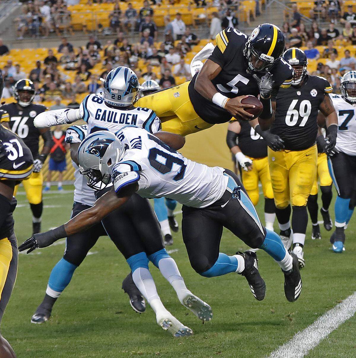 Pittsburgh Steelers quarterback Joshua Dobbs (5) leaps over Carolina Panthers defensive back Rashaan Gaulden (28) and defensive end Daeshon Hall (94) for a touchdown during the first half of a preseason NFL football game in Pittsburgh, Thursday, Aug. 30, 2018. (AP Photo/Keith Srakocic)