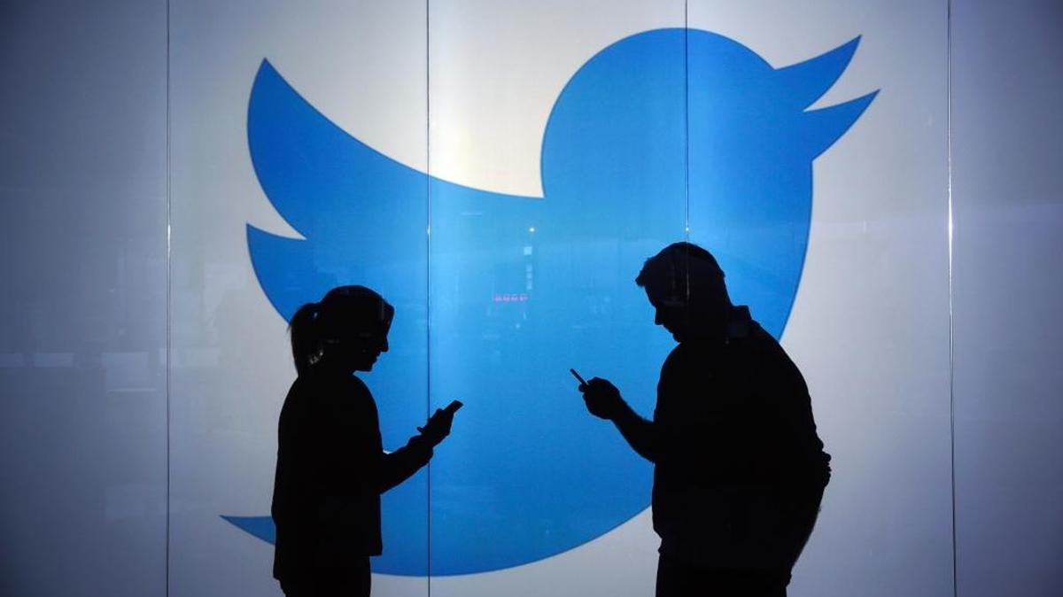 People are seen as silhouettes as they check mobile devices whilst standing against an illuminated wall bearing Twitter Inc.'s logo in this arranged photograph in London, U.K., on Jan. 5, 2016.