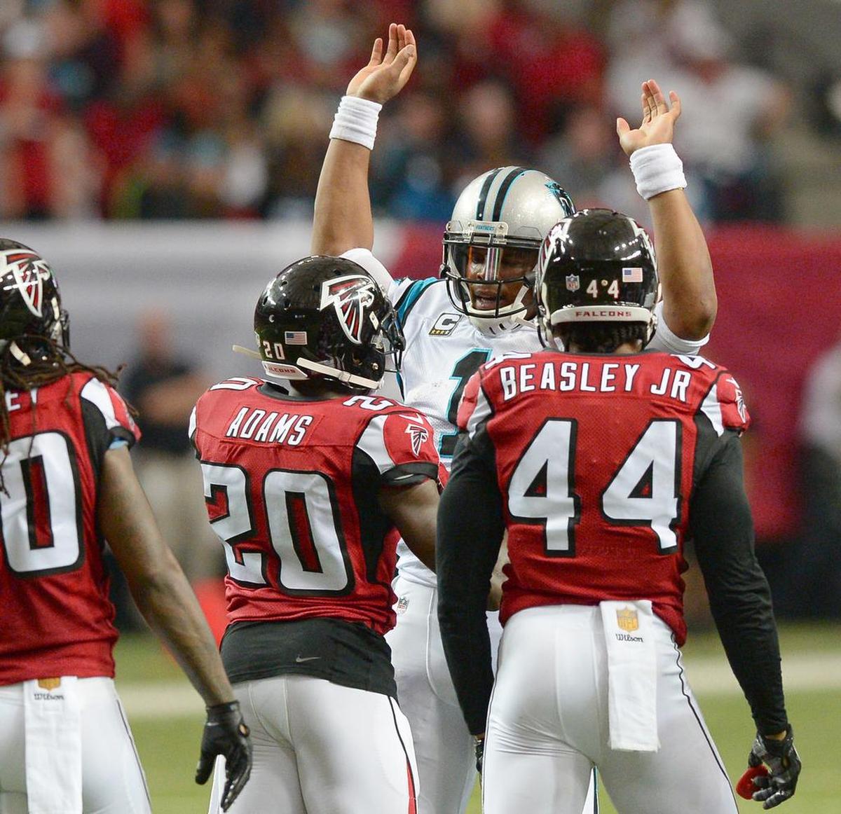 Carolina Panthers quarterback Cam Newton raises his arms as Atlanta Falcons cornerback Phillip Adams and linebacker Vic Beasley Jr. approach him after his rushing for yardage during first quarter action at the Georgia Dome on Sunday, December 27, 2015 in Atlanta, GA. The Falcons defeated the Panthers 20-13.