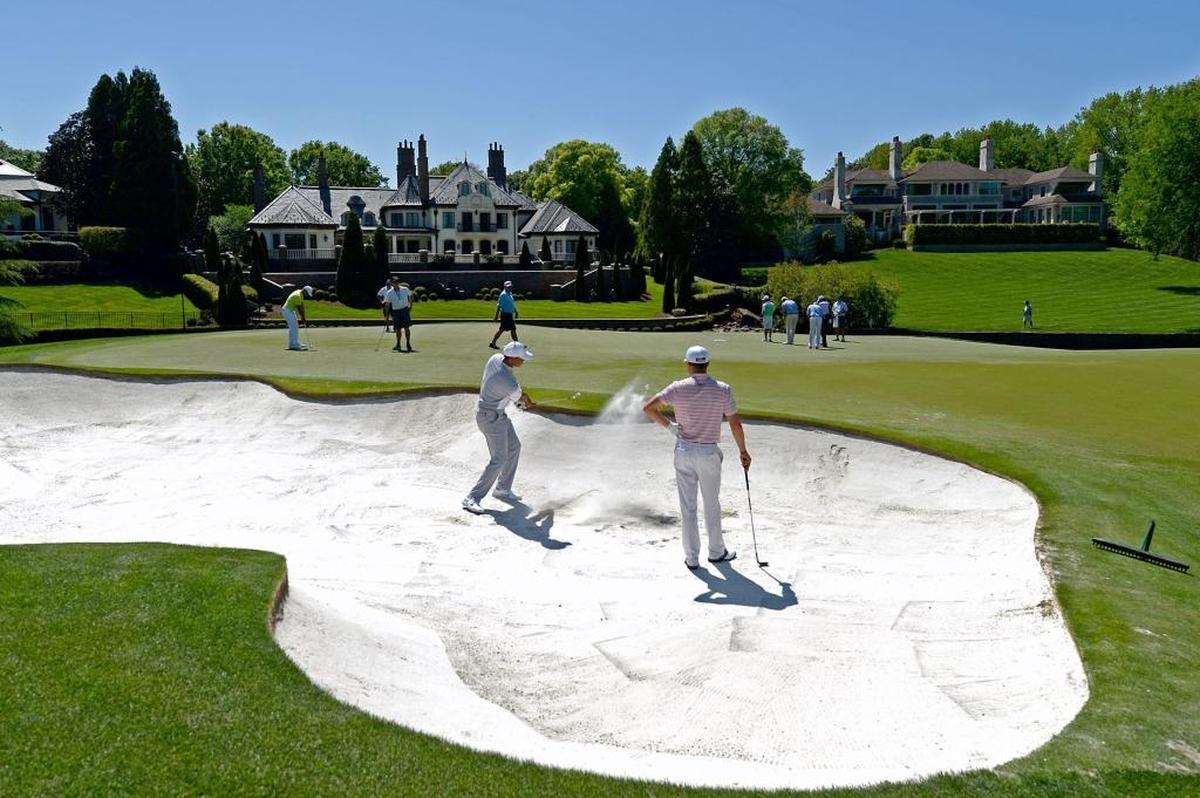 Tiger Woods, left, hits from a sand trap along the seventh green at Quail Hollow Club during Tuesday’s practice round. Playing partner Justin Thomas, who won the PGA Championship last August at Quail Hollow, looks on..