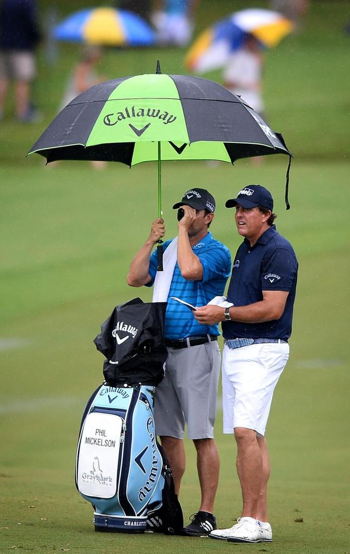 Phil Mickelson (right), trying to stay dry during Tuesday’s practice round at Quail Hollow, prepares for an approach shot at No. 5, a par-4, 449-yard hole.