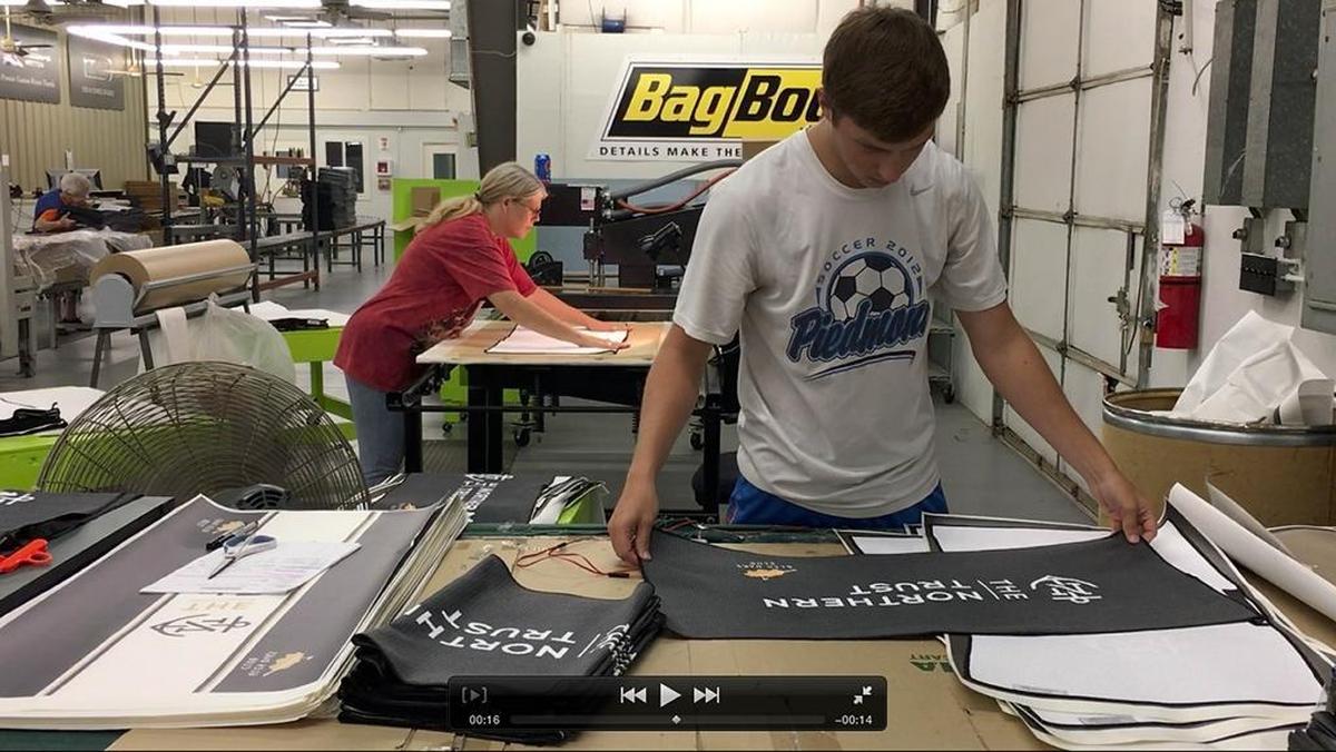 Ben Bullard, right, folds freshly printed towels as Angie Mullis, left, prints them while working at Devant Towels in Monroe on Wednesday. The company has produced a selection of towels for the upcoming PGA Championship in Charlotte.