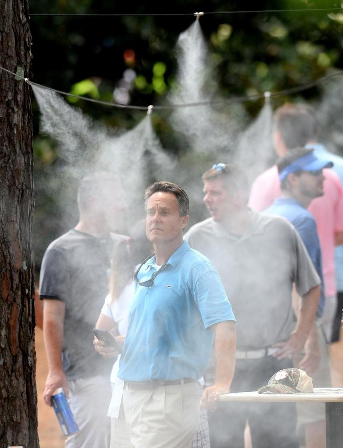 Charlotte golf fan Ed Barnes, left, cools down using a sprayer a sprayer at Quail Hollow. With temperatures and humidity rising, concession stands had longer lines than bathrooms much of Saturday afternoon.
