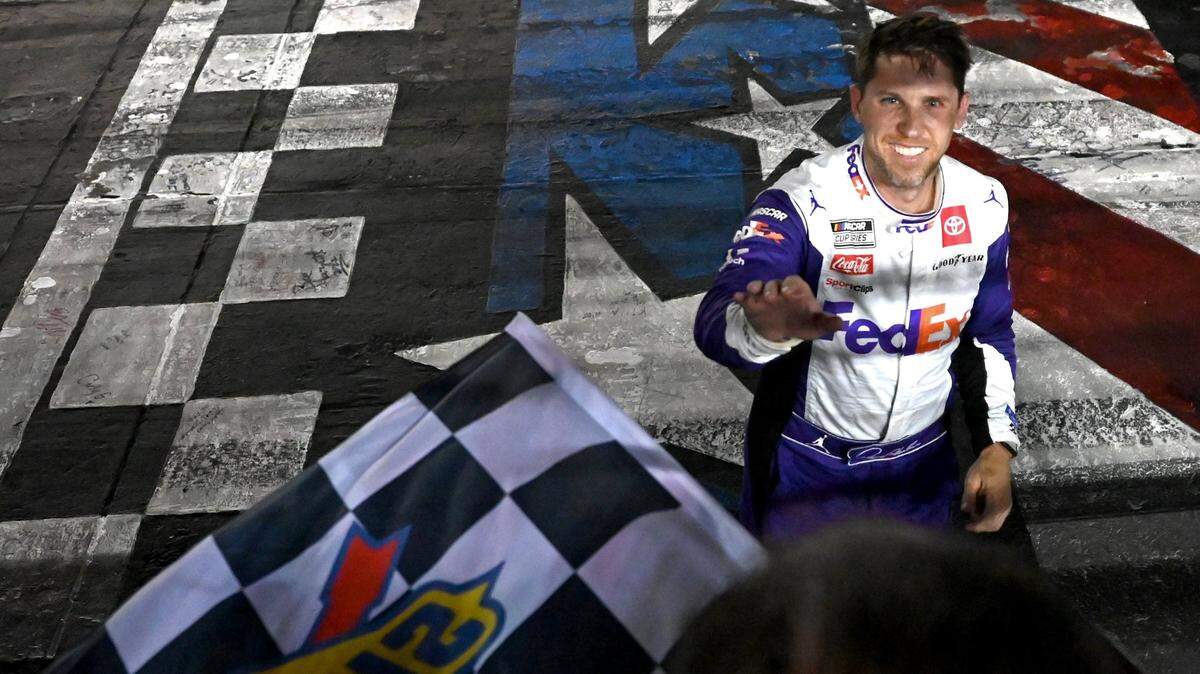 NASCAR driver Denny Hamlin smiles as he reaches out to take the checkered flag after winning the Coca-Cola 600 at Charlotte Motor Speedway on Sunday, May 29, 2022. Hamlin held off Kyle Busch for the victory.