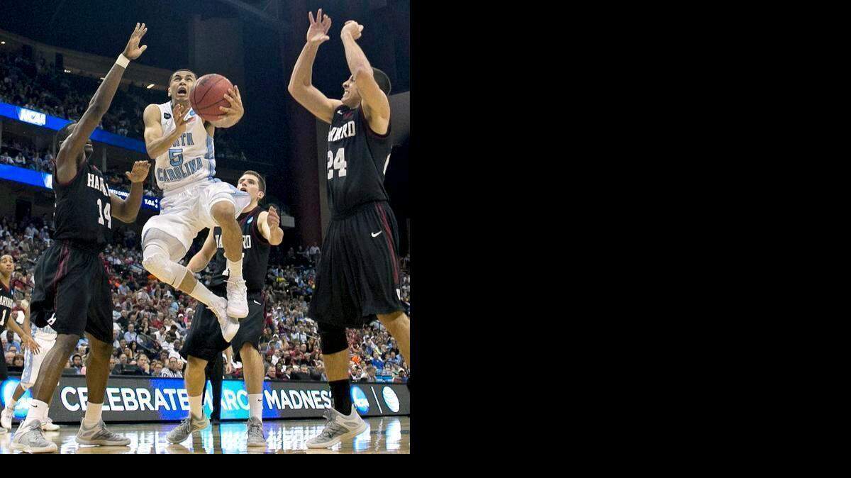 
North Carolina’s Marcus Paige drives to the basket between Harvard’s Steve Moundou-Missi (14) and Jonah Travis (24) for two of his 12 points during the second half of their second round game in the NCAA Tournament on Thursday, March 19, 2015, in Jacksonville, Fla.
