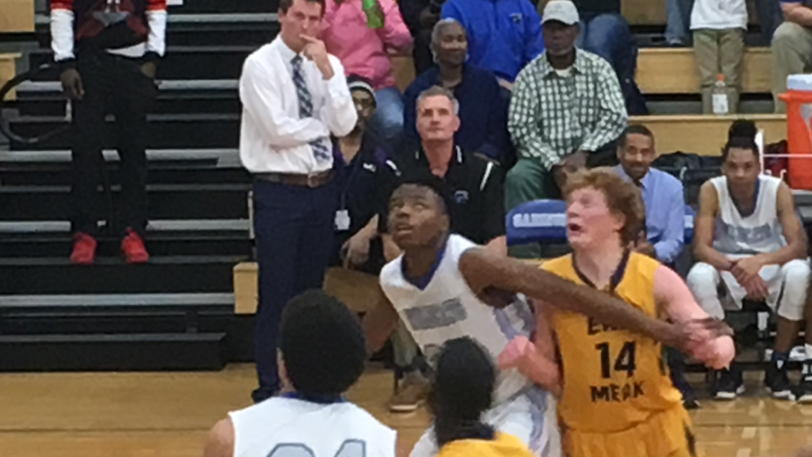 Christian Laettner (seated on bench) watches Garinger (in white) take on East Mecklenburg Friday night. Garinger head coach Jordan Yawn is standing beside Laettner.